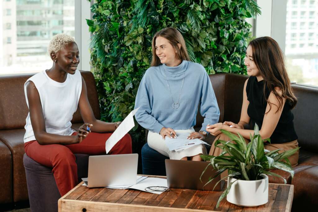 Three women sit around a plant in the office 
