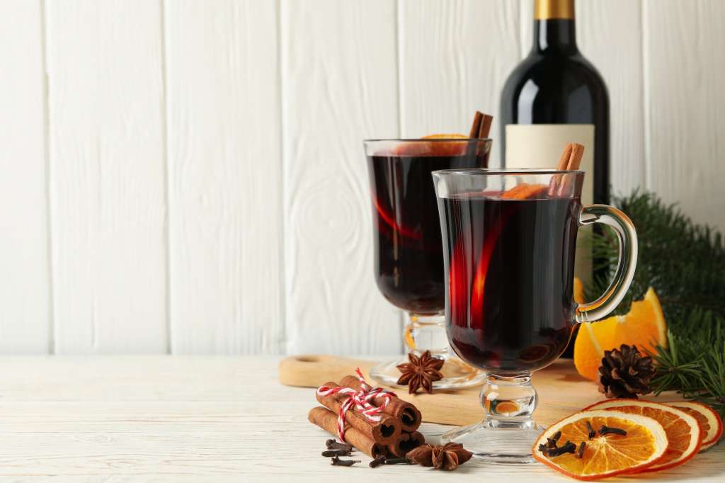 Bottle of wine, cups of mulled wine and ingredients on wooden background