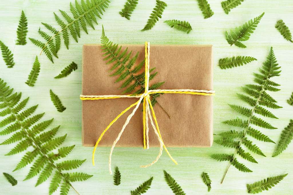 Gift box wrapped of craft paper and white and yellow ribbon on a green wooden background decorated