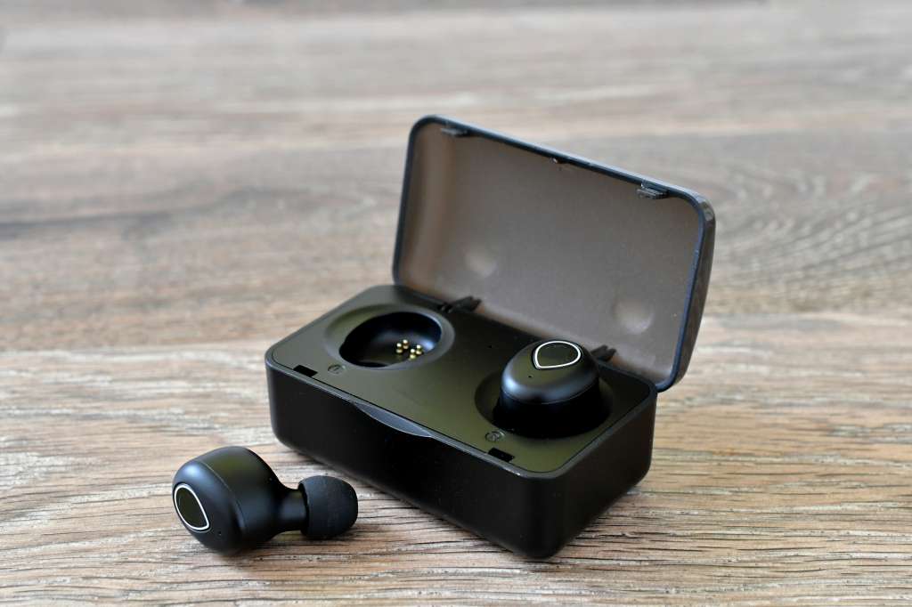 Generic Black wireless earbuds in a charging case on a wood background. (logos and labels removed)