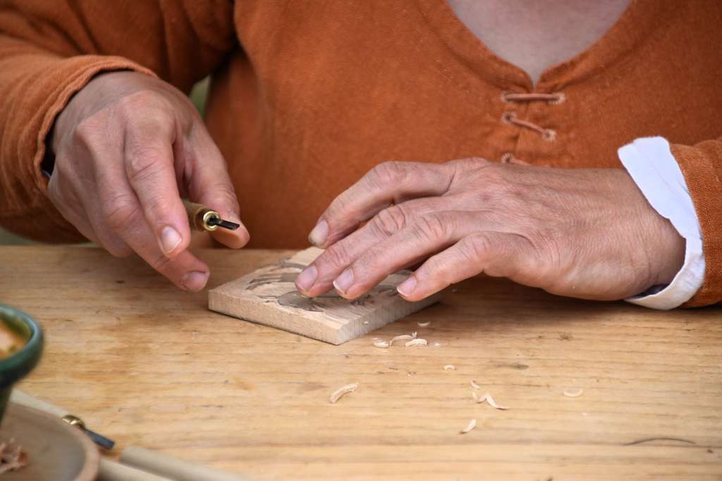 female caucasian hands carving some wood with a tool on a wooden table