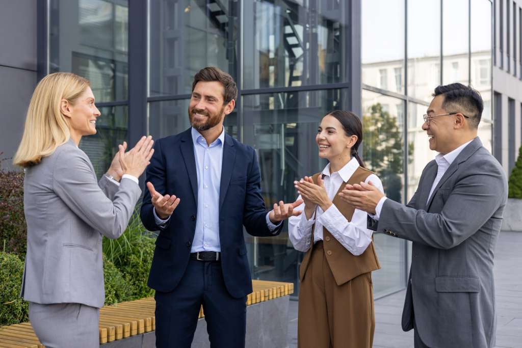 Business people outside office building applauding and congratulating colleague boss with promotion